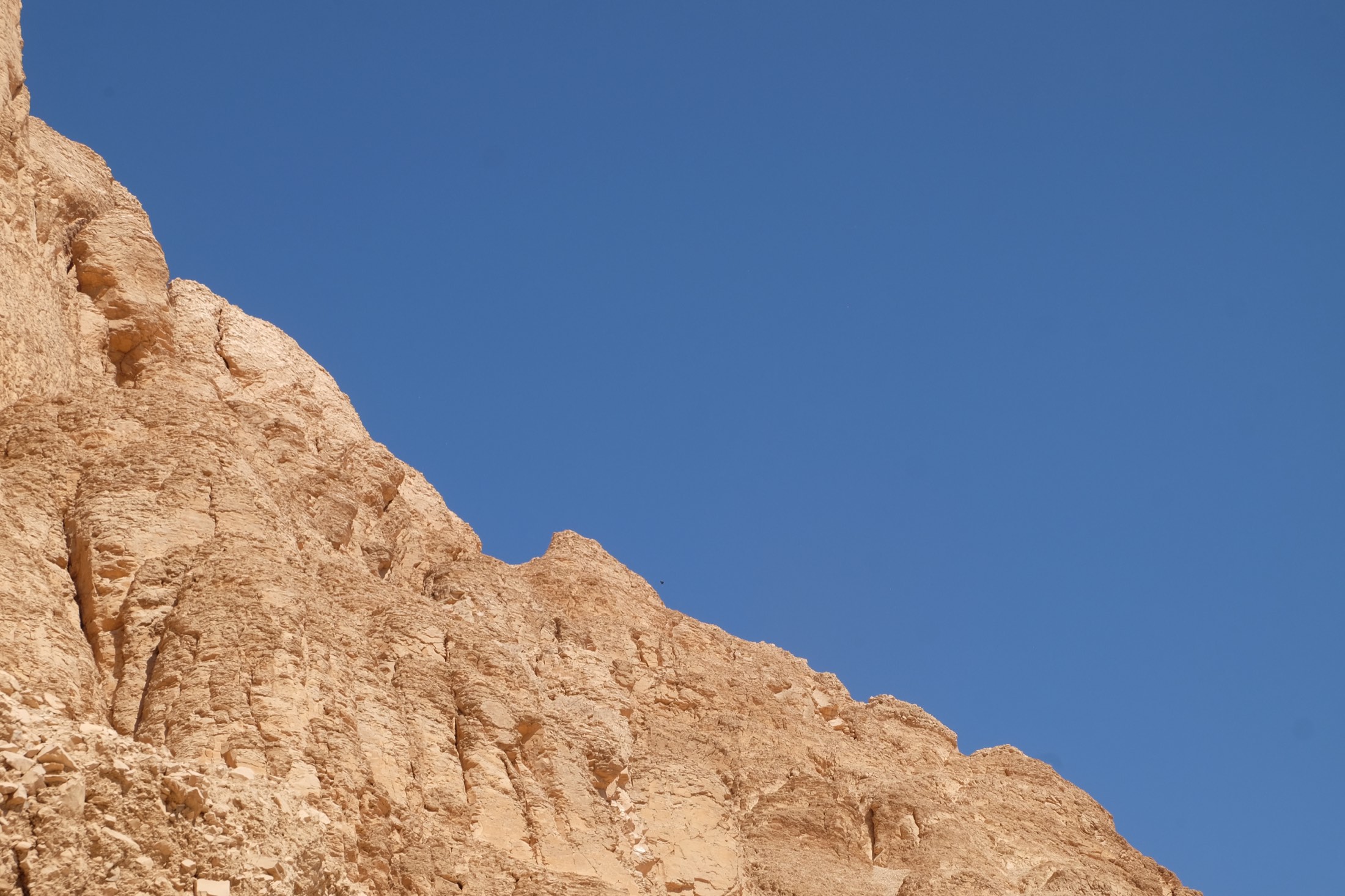 Sunlit desert cliff face against a deep blue sky, West Bank of Luxor